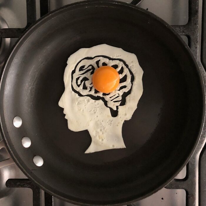 Creative egg art featuring a fried egg shaped like a human head with a brain design, yolk resembling the brain surface.