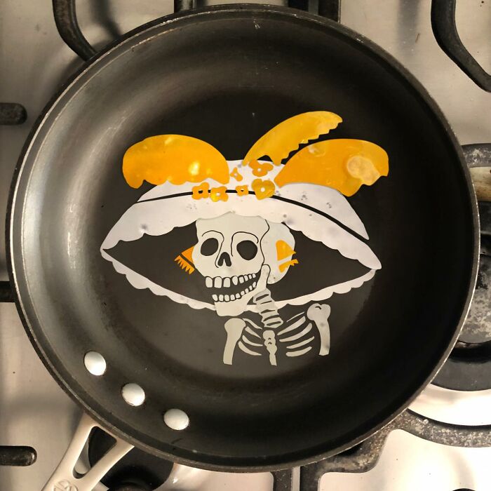 Creative egg art in a frying pan depicting a skeleton wearing a hat.