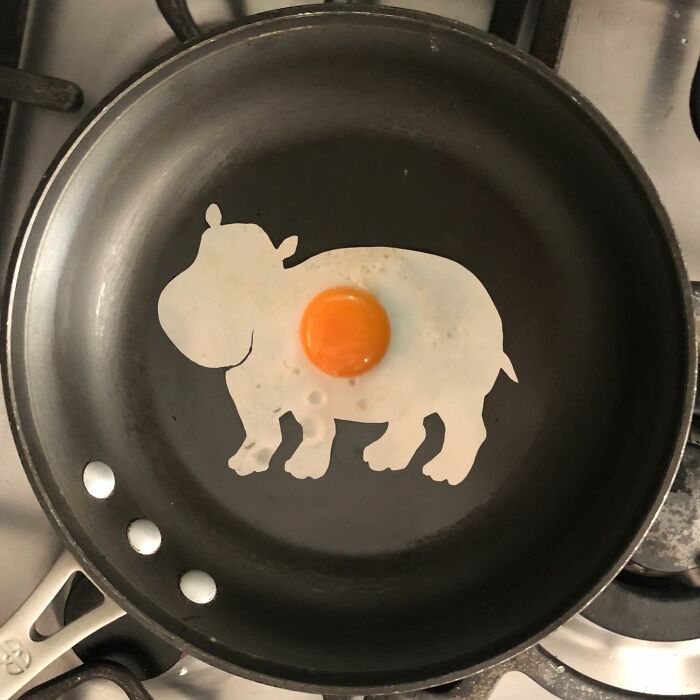 Creative egg art in a frying pan shaped like a hippopotamus using a fried egg.