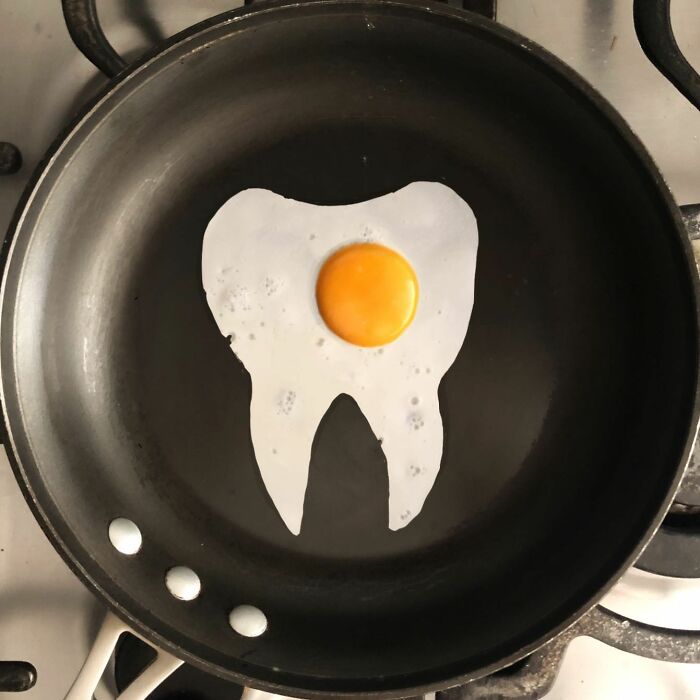 Creative fried egg art shaped like a tooth in a frying pan.