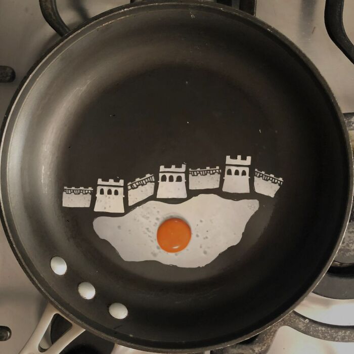 Creative egg art with yolk as sun over a painted castle scene in a frying pan.