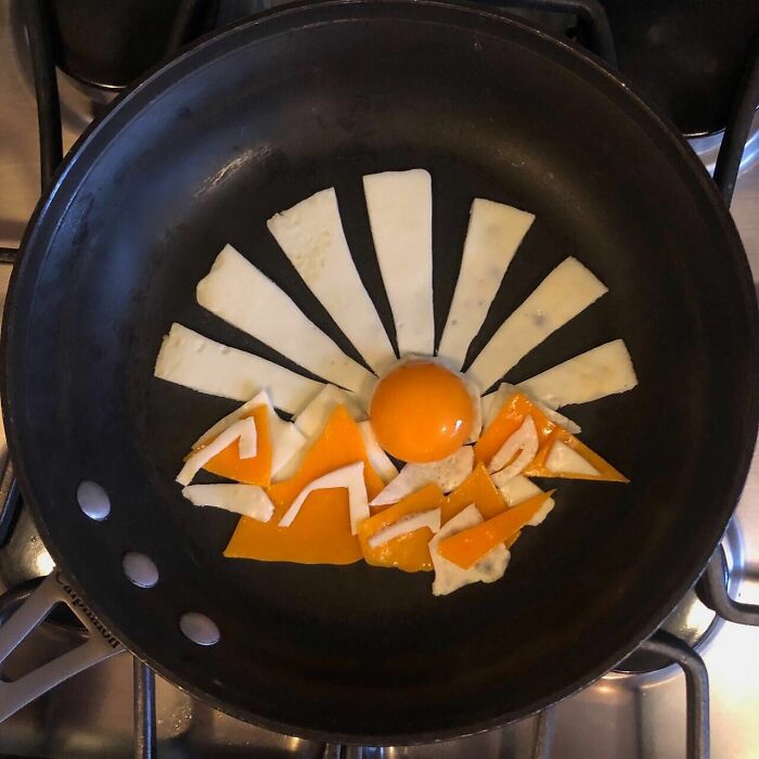 Creative fried eggs arranged as sun and mountains in a frying pan.