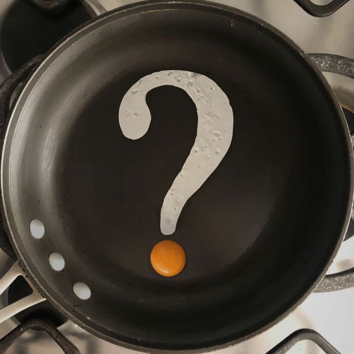 Creative egg art with fried egg whites forming a question mark and yolk as the dot in a frying pan.