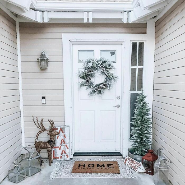 Front porch Christmas decorating ideas with wreath, mini tree, and reindeer by a white door.