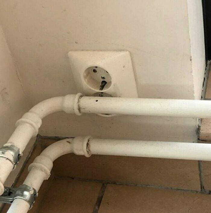 Construction fail with pipes installed blocking an electrical outlet on a tiled wall.