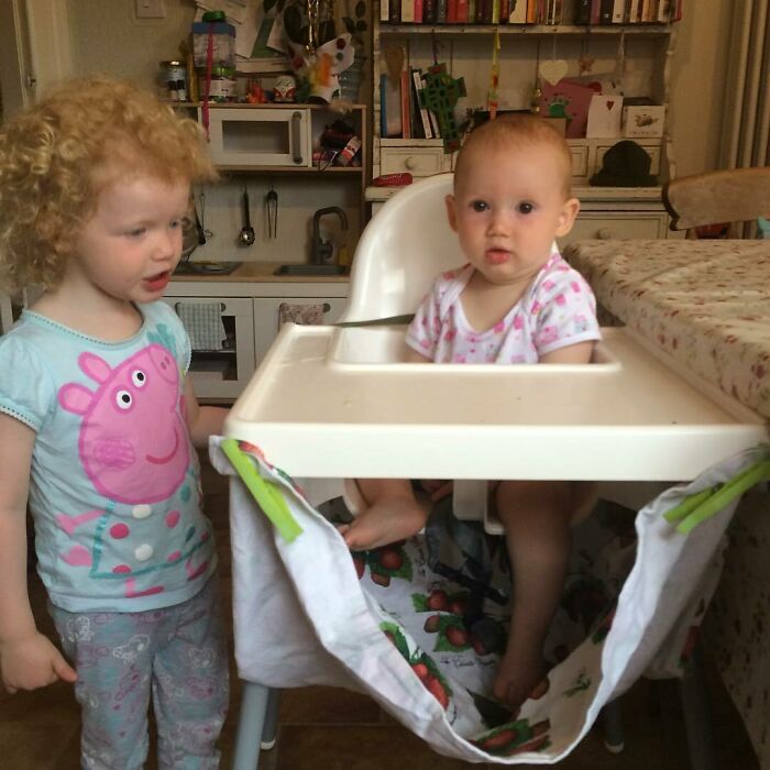 Two young children in a kitchen with a clever parenting trick using a high chair and cloth as a catch-all solution.