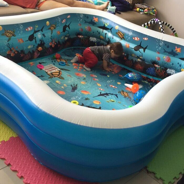 A toddler playing in a large inflatable pool indoors, showcasing parenting genius tricks for safe play.