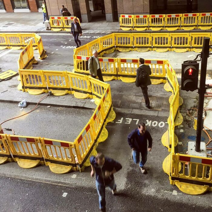 People walking through a maze of yellow barriers on a street, resembling a scene from videogames.