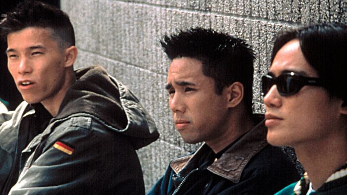 Three men in casual jackets sitting against a wall, embodying fascinating fan theories discussion.