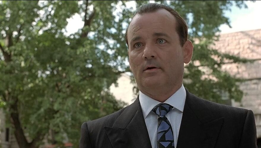 Actor Bill Murray in a suit outdoors with trees in the background, showcasing a classic performance style consistent with their roles.