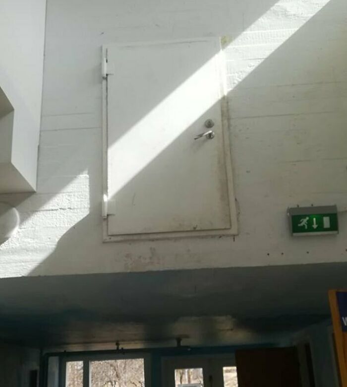 Construction fail: A door installed high on a wall without access, next to an exit sign.