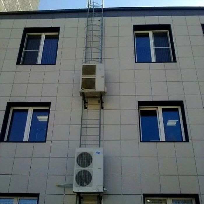 Air conditioning unit awkwardly mounted between windows on building facade, showcasing construction mishap.