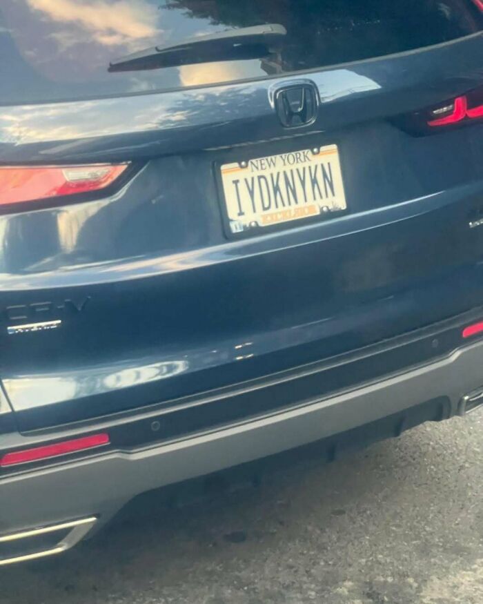 New York funny license plate reads "IYDKNYKN" on a blue Honda CR-V, parked on a city street.