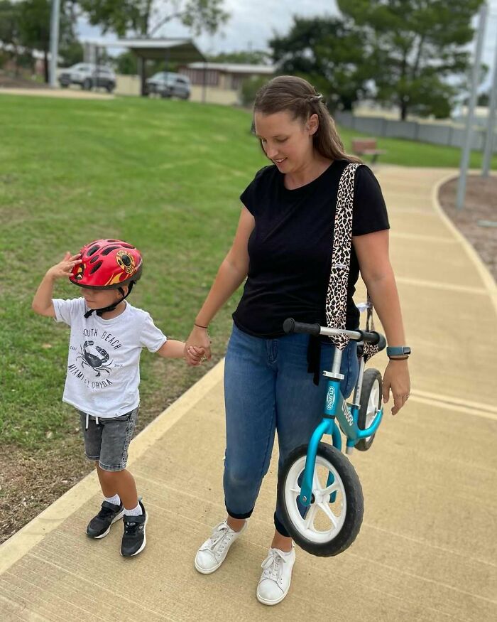 Woman using parenting genius tricks by carrying a balance bike while holding her child's hand.