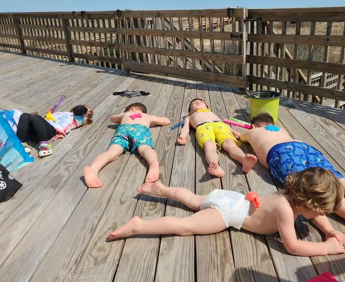 Children napping on a wooden deck with toys, using a parenting genius trick to relax outdoors.