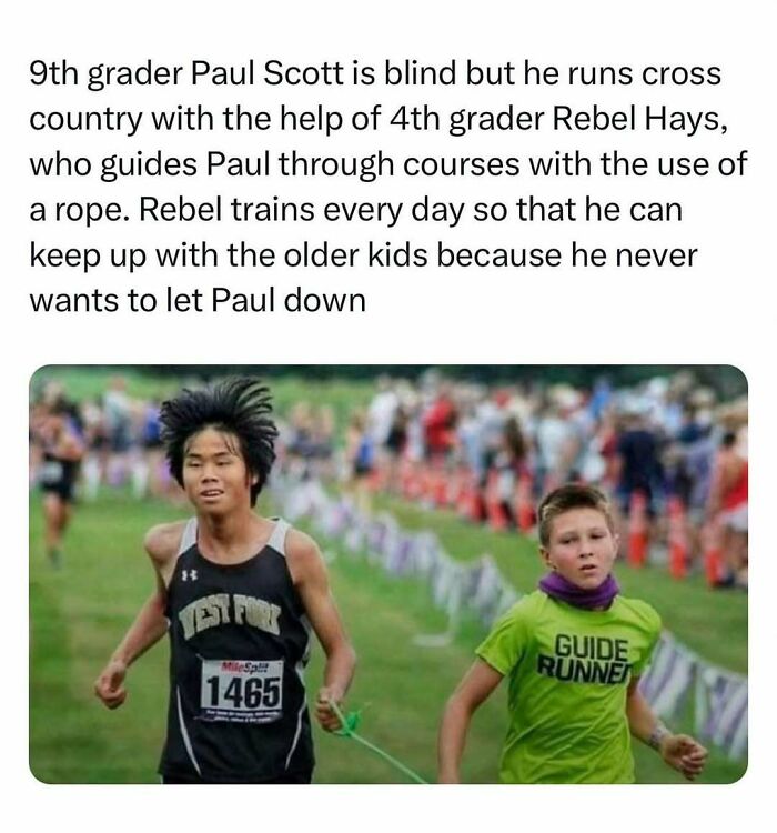 Two boys running in a cross country race, showcasing wholesome-kindness, one guiding the other with a rope.