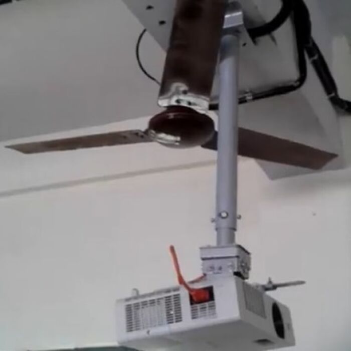 Ceiling fan hilariously installed intersecting with a projector, displaying a construction fail.