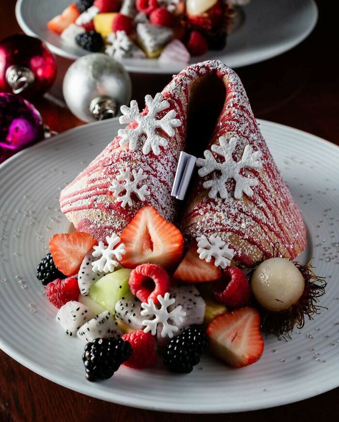 Festive Christmas snack with fruit, snowflake decorations, and colorful holiday ornaments on a white plate.