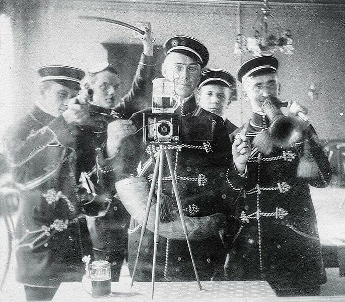 Vintage group photo with historical uniforms, men posing with a camera, trumpet, and sword, reflecting on the past.