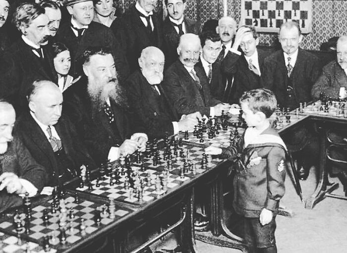 Young boy playing simultaneous chess matches against adults, showcasing historical moments to shape the future strategies.