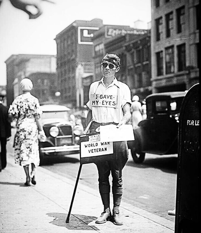 World War I veteran wearing a sign, standing on a city street, highlighting historical impacts on future perspectives.