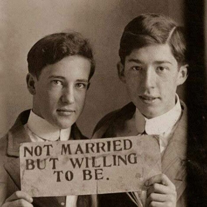 Two young men from the past holding a sign that reads "Not married but willing to be", showcasing historical moments.