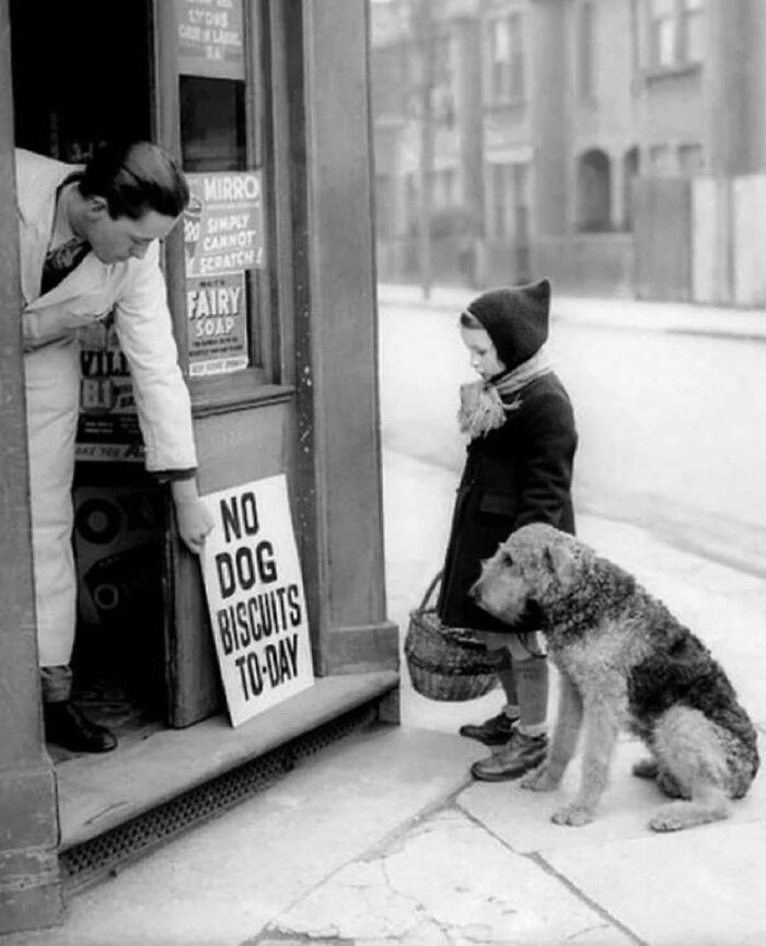 A child with a dog outside a shop displaying a "No Dog Biscuits Today" sign; a glimpse into historical daily life.