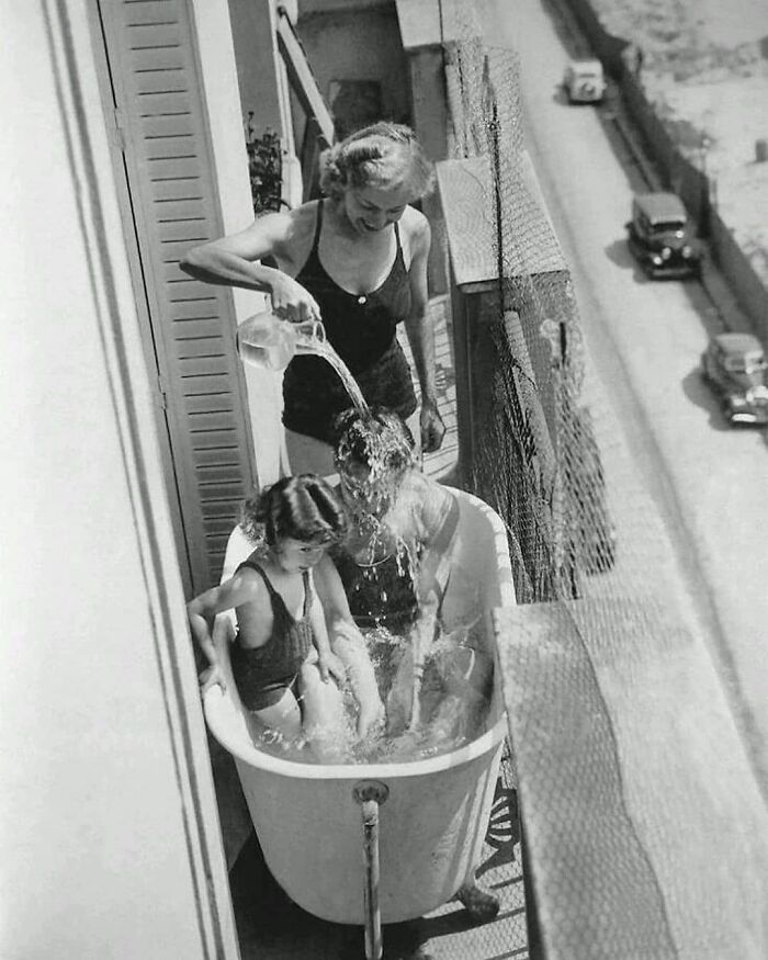 Historical picture of a woman bathing a child on a balcony in a vintage tub, showcasing past living styles.