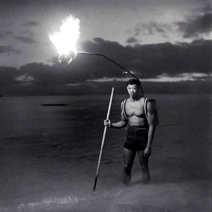 Man holding a burning torch at the beach during sunset, capturing a historical moment.