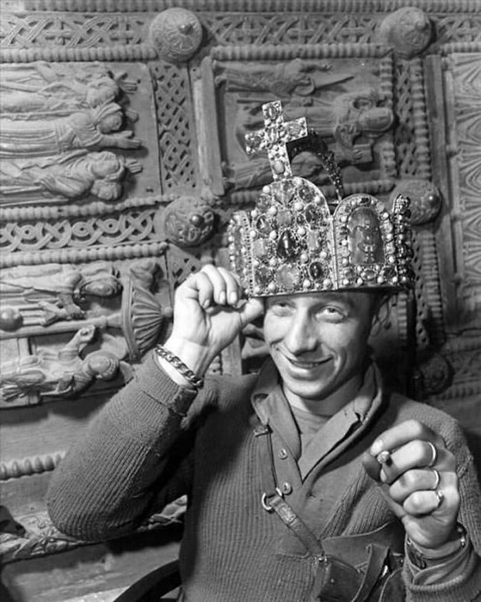 Person wearing an ornate crown, smiling in front of a historical relief, representing past influences on the future.