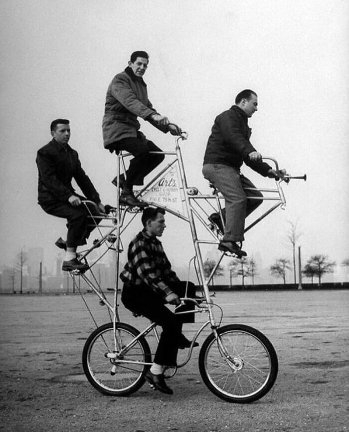 Four men riding a multi-level bicycle in a vintage black and white photograph, showcasing historical ingenuity.