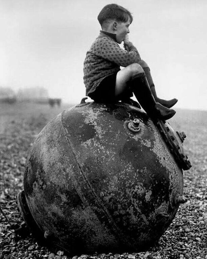 Child sitting on a large, rusted WWII sea mine, reflecting on history's impact on the present and future.