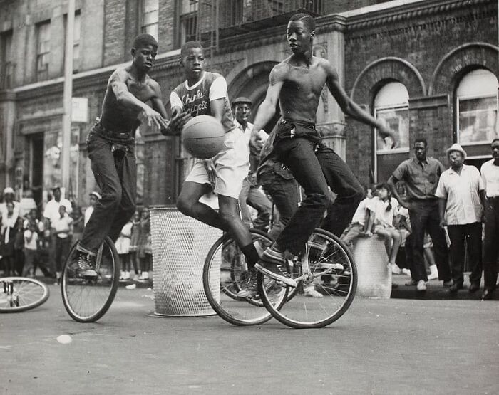 Historical picture of street performers riding unicycles and playing basketball in an urban setting.