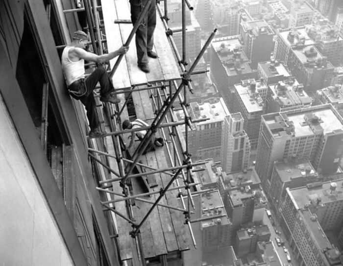 Construction workers on scaffolding above a city skyline, embodying historical resilience and innovation.