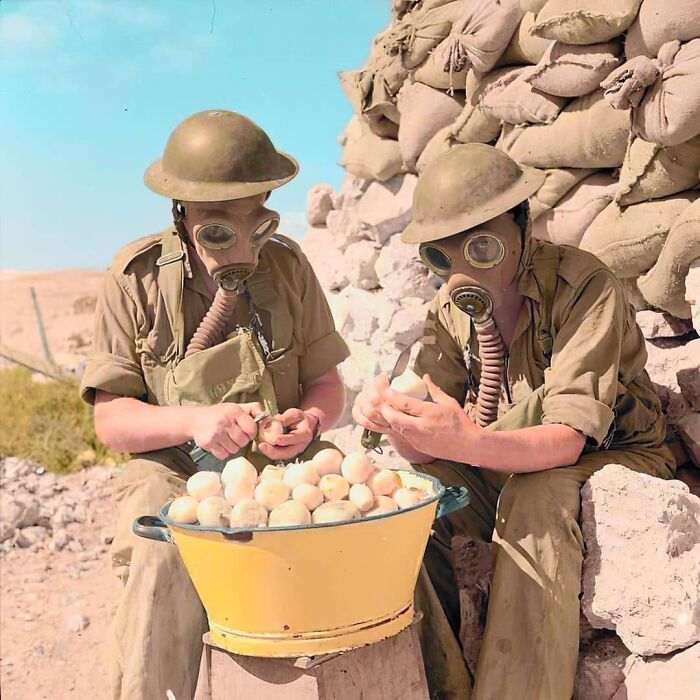 Soldiers in gas masks peeling potatoes by sandbags, showcasing historical moments from a dedicated IG page.