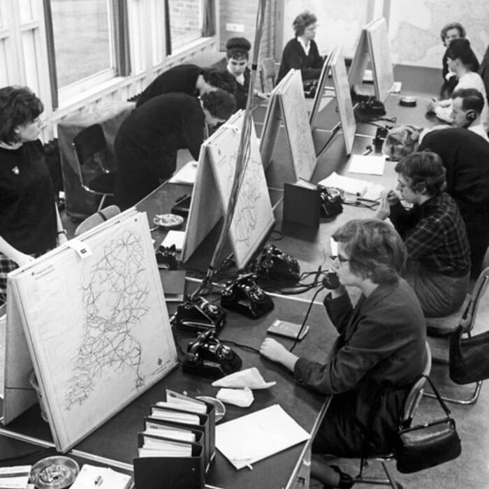 People working at a historical telephone exchange, using maps and vintage phones to manage calls.