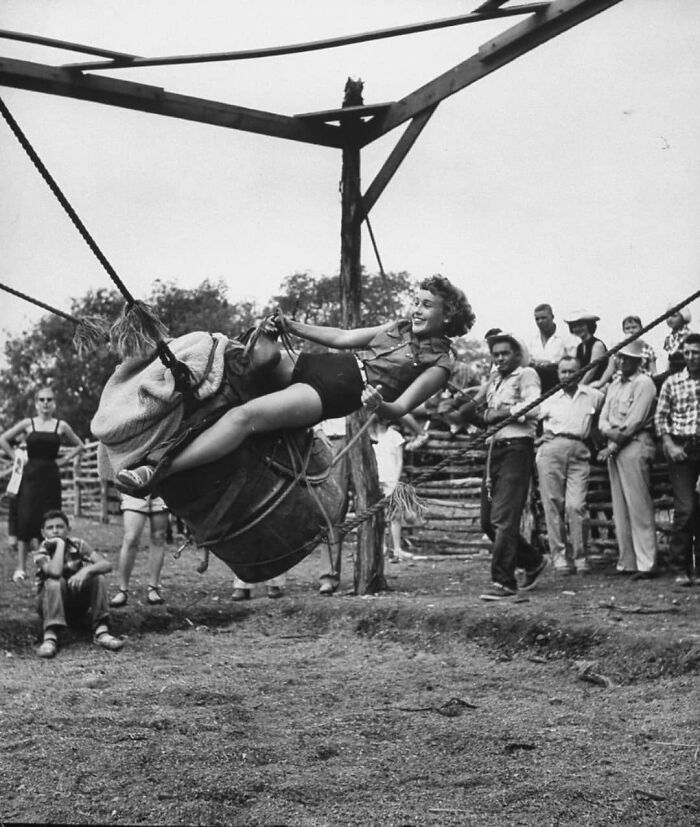 Woman enjoying a historical swing ride, surrounded by onlookers at an outdoor event.