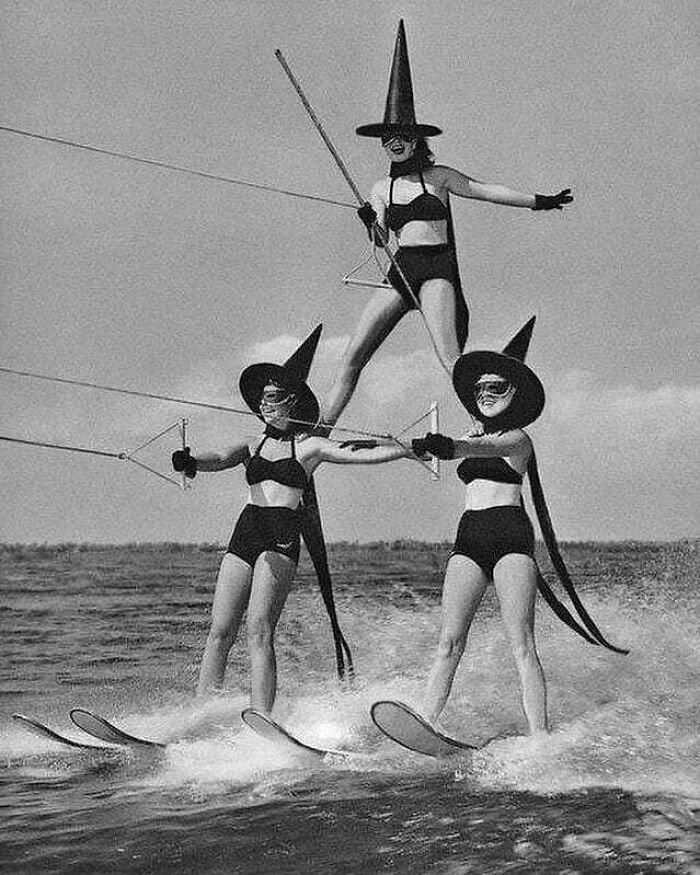 Three women in witch hats perform acrobatic water-skiing, showcasing a historical moment of creativity and skill.