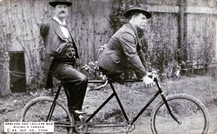 Two men on a tandem bicycle, one armless and the other legless, showcasing historical innovations in mobility.