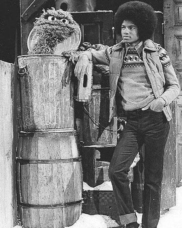 Person beside Oscar the Grouch on "Sesame Street" set in historic black-and-white photo, embracing the past.