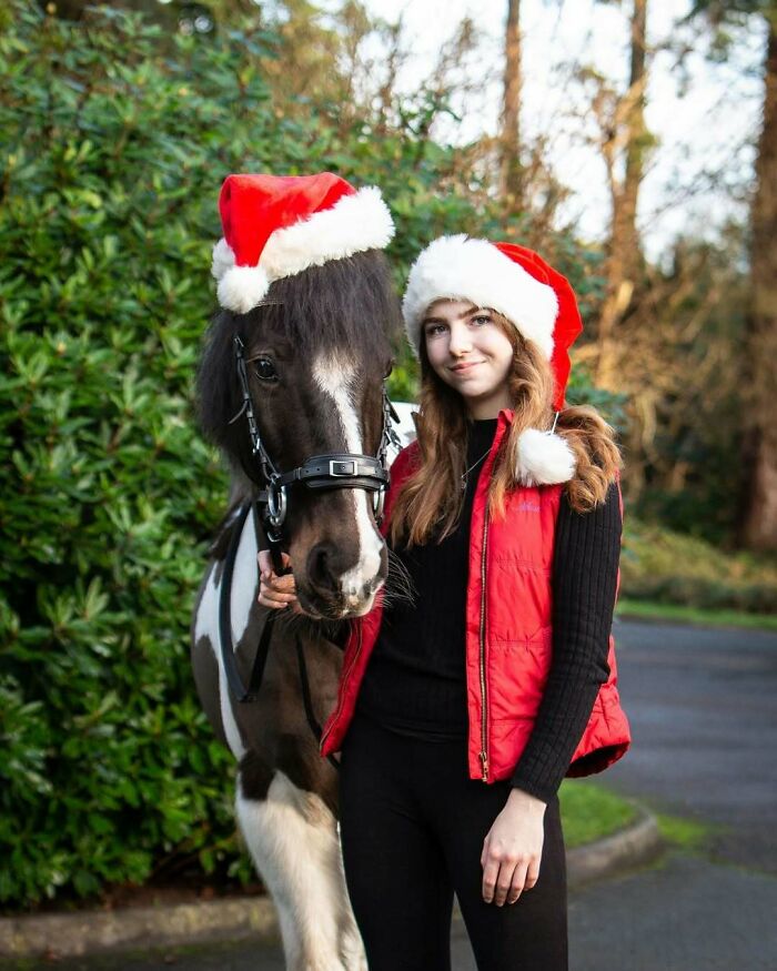 Girl with a horse wearing Santa hats, enjoying Christmas together outdoors. Cute funny Christmas animals theme.