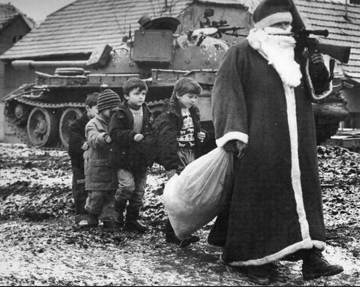 Santa with rifle, leading children past a tank in historical photo, illustrating how we can learn from the past.