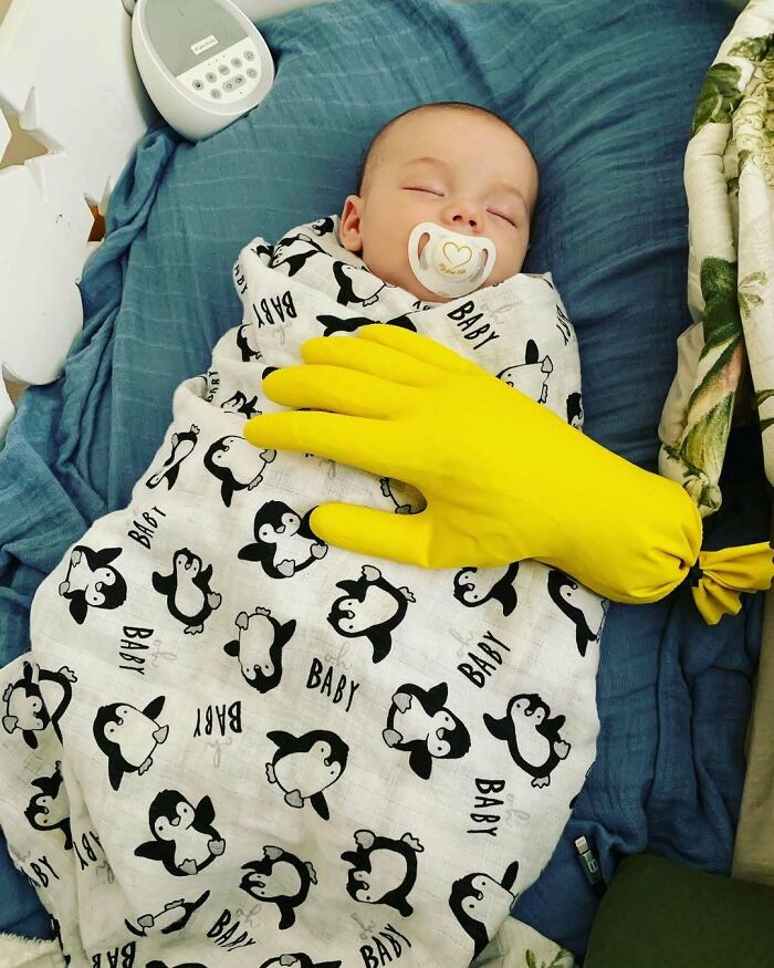 Sleeping baby in penguin blanket with yellow glove trick, showcasing parenting genius tricks.