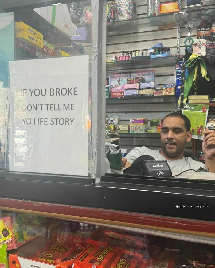 Man in a store with humorous "If you're broke don't tell me your life story" sign, embodying New York humor.