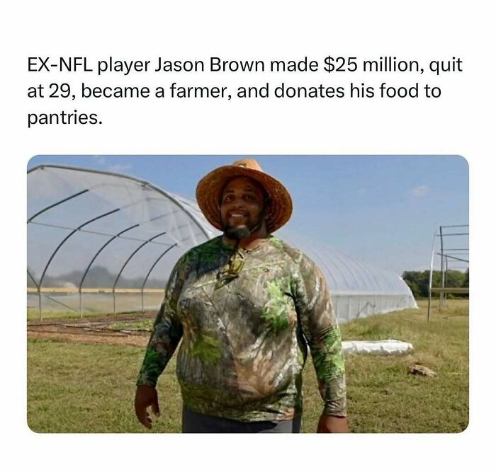 Man in a camo shirt and straw hat stands smiling on a farm next to a greenhouse, illustrating wholesome kindness.