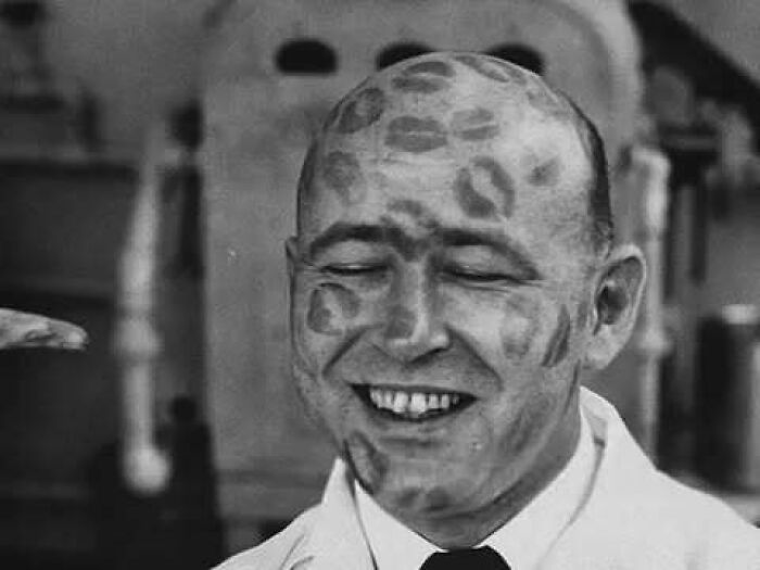 Smiling man with kiss marks on his head, showcasing a quirky moment from the past for historical reflection.