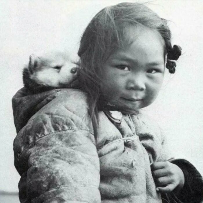 Young girl in a winter coat with a sleeping puppy on her shoulder, embodying historical moments from the past.