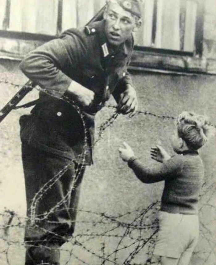 Soldier helps child over barbed wire, showcasing interesting history facts.