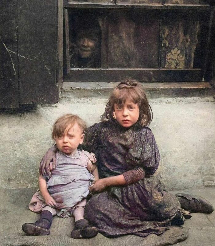 Two children sitting on the ground with a person peering from a window, showcasing interesting historical context and facts.