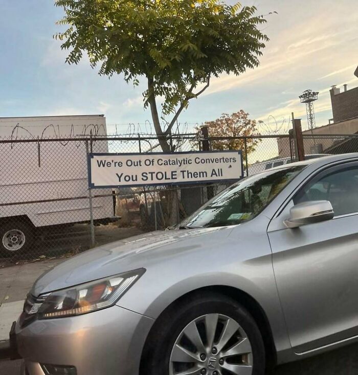 Silver car with a sign about stolen catalytic converters, capturing the humorous side of New York issues.